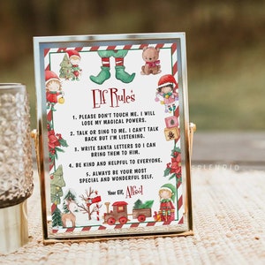 May include: A rectangular gold-toned metal frame containing a white sign titled Elf Rules. The sign features watercolor illustrations of elves, a train, and a reindeer, with five numbered rules and the signature Your Elf, Alfsól printed in black.