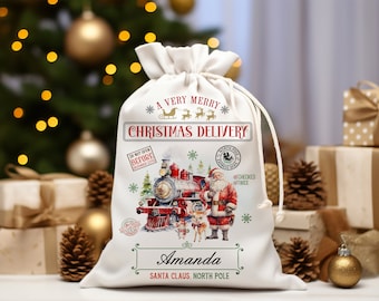 May include: A white canvas gift bag with a red and green Christmas design featuring a train, Santa Claus, and reindeer. The bag has the text "A Very Merry Christmas Delivery" and "Santa Claus, North Pole" printed on it. The bag is personalized with the name "Amanda".