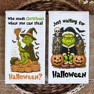 May include: Two white waffle-weave kitchen towels with Halloween designs. One shows a green character in a witch hat, with the text "Who Needs Christmas When you can steal Halloween?" The other shows a green character in a Santa hat, with the text "Just waiting for Halloween."