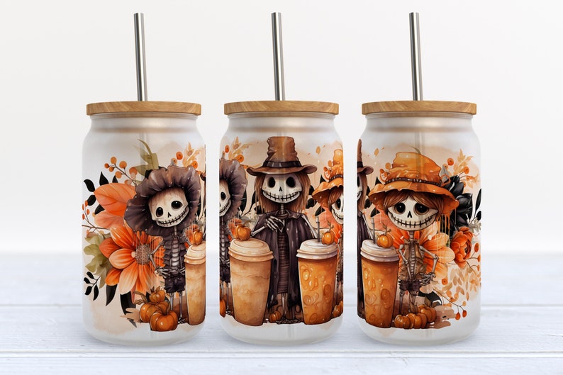 May include: Three frosted glass can-shaped tumblers with bamboo lids and metal straws. Each features a printed illustration of skeletons wearing hats, surrounded by orange flowers and pumpkins in a fall-themed color palette.