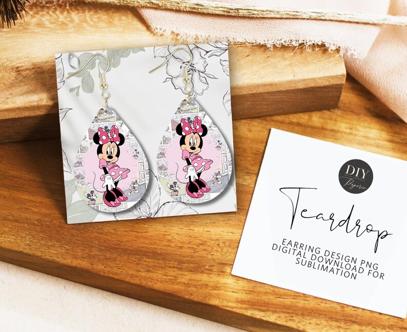 Op de afbeelding: Druppelvormige oorbellen met een Minnie Mouse-ontwerp. De oorbellen hebben een roze en zwart kleurenschema, met een cartoonafbeelding van Minnie Mouse. De oorbellen worden gepresenteerd op een witte kaart met bloemaccenten.