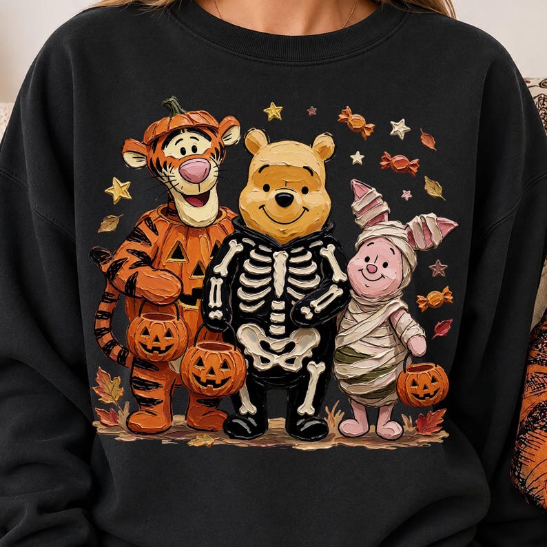 May include: A black crewneck sweatshirt featuring a graphic of Tigger dressed as a pumpkin, Winnie the Pooh wearing a skeleton costume, and Piglet wrapped as a mummy. The characters are holding small jack-o'-lantern buckets amidst falling autumn leaves, stars, and wrapped candies.