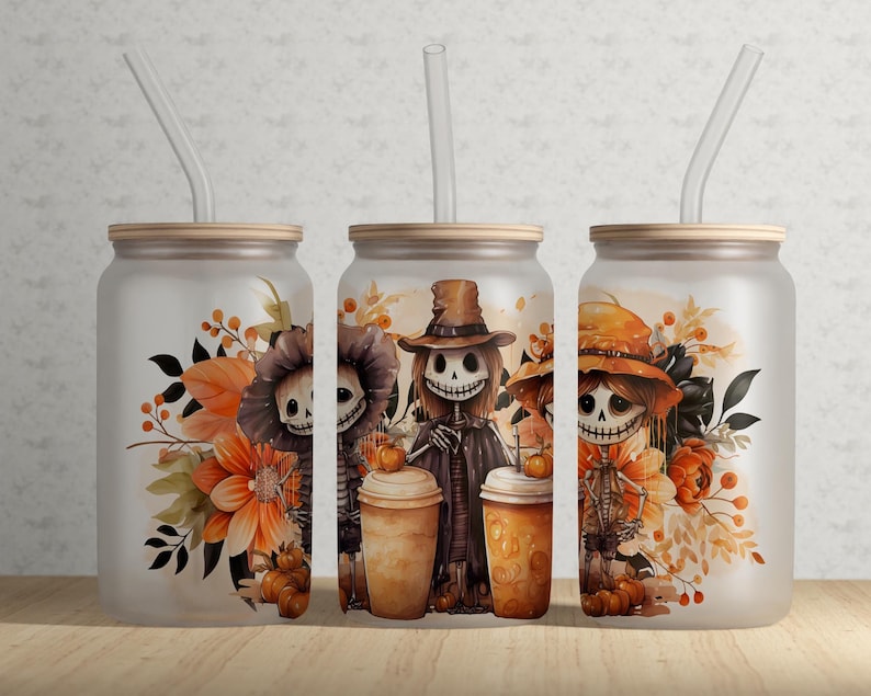 May include: Three frosted glass tumblers with bamboo lids and clear glass straws, each featuring a colorful illustration of skeletons wearing hats, surrounded by autumn flowers, orange leaves, and small pumpkins in a fall-themed design.