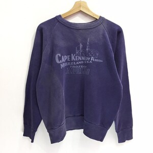 May include: A navy blue sweatshirt with long sleeves and a crew neck. The front features a faded print that reads "Cape Kennedy Florida Missileland USA Project Apollo". The sweatshirt is hanging on a wooden hanger against a white background.