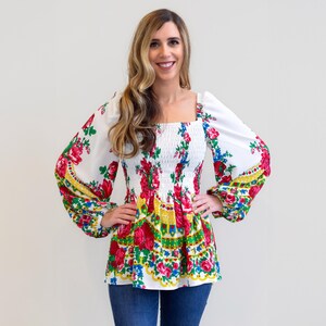May include: A white blouse with a floral print and a gathered elastic waistband. The sleeves are long and puffy.