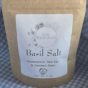 May include: A brown paper bag with a white label displaying "Basil Salt." The label states "Ingredients: Sea Salt & Organic Basil" and "Net Wt 2 oz." The label also features a floral design and the words "330 Homestead Oklahoma".