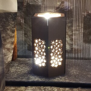 May include: A black hexagonal lamp with a geometric pattern cut out, illuminating a warm light.