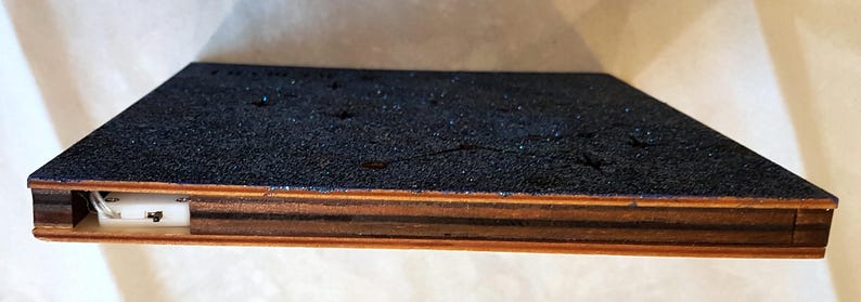 Puede incluir: Una caja de madera con una tapa de brillantina azul y un interruptor blanco en el lateral. La caja tiene un marco de madera oscura.