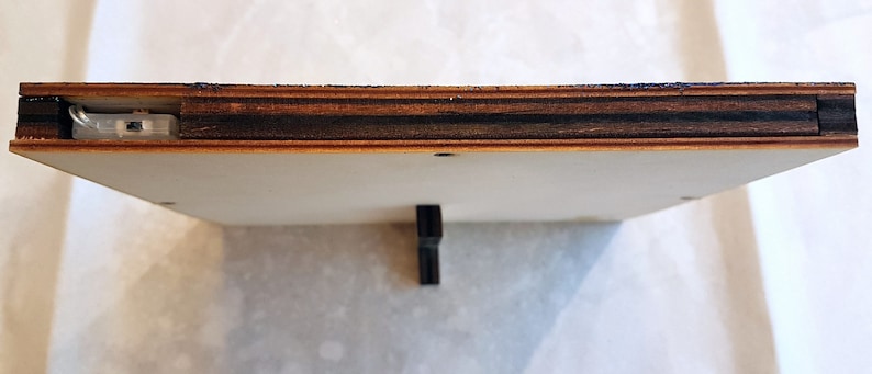 Puede incluir: Primer plano de la parte inferior de un marco de madera. El marco est&aacute; hecho de madera contrachapada con una chapa de madera oscura. Una peque&ntilde;a pieza de metal es visible en la parte superior central del marco.