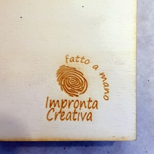 Puede incluir: Un letrero de madera con un dise&ntilde;o de huella digital marr&oacute;n y el texto "fatto a mano" (italiano para "hecho a mano") e "Impronta Creativa" (italiano para "Huella Creativa").