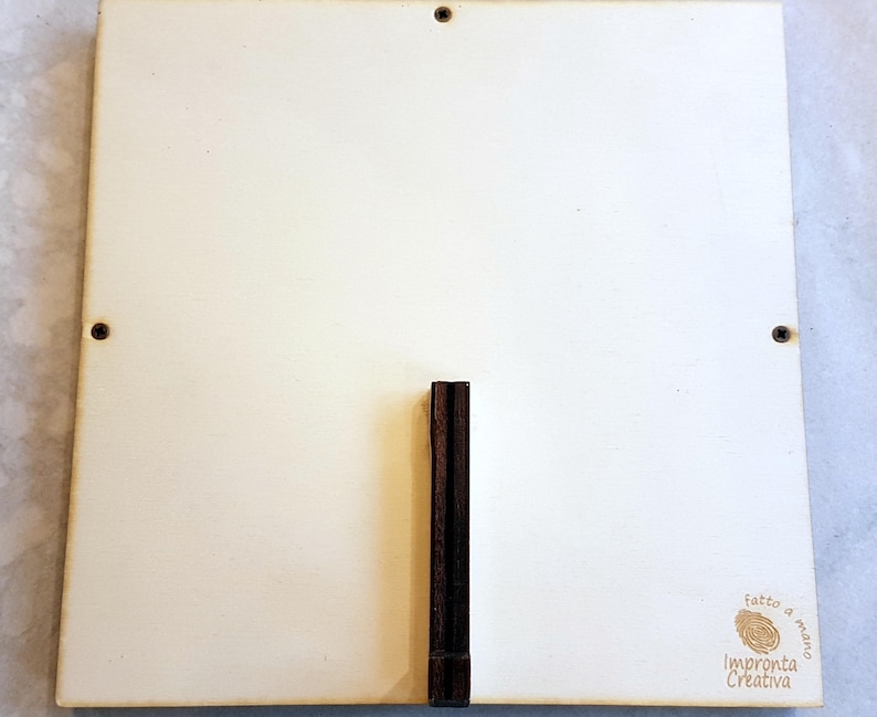 Puede incluir: Un letrero cuadrado de madera blanca con un soporte de madera marr&oacute;n. El letrero tiene un peque&ntilde;o sello marr&oacute;n que dice "fatto a mano" e "Impronta Creativa".
