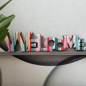 WELCOME. Allegra decorazione per la casa. Cartone decorato a strisce multicolori. Appendere al muro o appoggiare su un mobile. Leggerissima