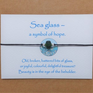 May include: A black string bracelet with a green sea glass bead and a silver bead. The bracelet is on a white card with the text "Sea glass - a symbol of hope. Old, broken, battered bits of glass, or joyful, colourful, delightful treasure? Beauty is in the eye of the beholder."