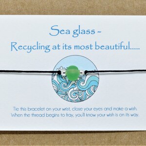 May include: A green sea glass charm bracelet with black string and a wave design on the card. The card reads "Sea glass - Recycling at its most beautiful.... Tie this bracelet on your wrist, close your eyes and make a wish. When the thread begins to fray, you'll know your wish is on its way."