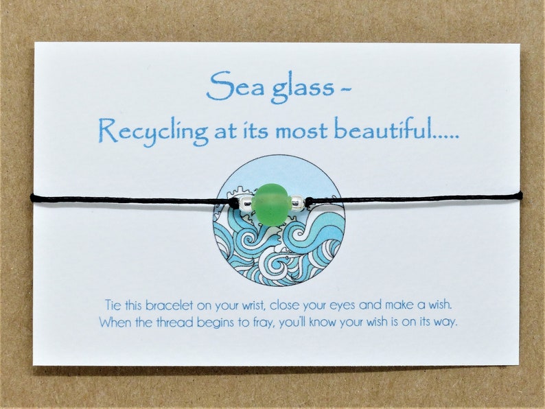 May include: A green sea glass charm bracelet with black string and a wave design on the card. The card reads "Sea glass - Recycling at its most beautiful.... Tie this bracelet on your wrist, close your eyes and make a wish. When the thread begins to fray, you'll know your wish is on its way."