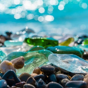 May include: Close-up of smooth, colorful sea glass and gray pebbles on a beach. The sea glass is various shades of blue, green, and clear. The pebbles are smooth and gray.