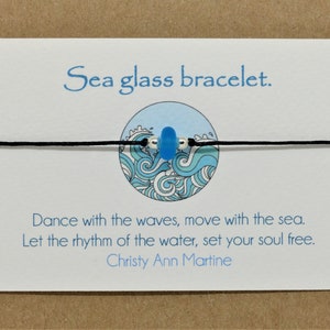 May include: A sea glass bracelet with a blue sea glass bead on a black cord. The card reads "Sea glass bracelet. Dance with the waves, move with the sea. Let the rhythm of the water, set your soul free. Christy Ann Martine."