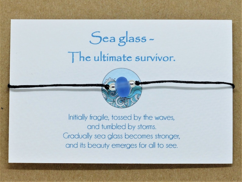 May include: A blue sea glass charm on a black cord bracelet with a white card that reads "Sea glass - The ultimate survivor. Initially fragile, tossed by the waves, and tumbled by storms. Gradually sea glass becomes stronger, and its beauty emerges for all to see."
