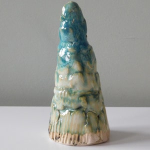 May include: A ceramic sculpture in the shape of a cone with a textured surface. The sculpture is glazed in shades of blue, green, and white.