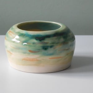 May include: A small, white ceramic bowl with a green and yellow glaze. The glaze has a swirling pattern, creating a unique and artistic look.