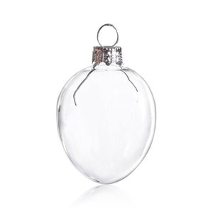 Puede incluir: Un adorno de vidrio transparente con una parte superior de metal plateado. El adorno tiene forma de corazón y es perfecto para agregar un toque de elegancia a tu árbol de Navidad.