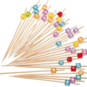 Op de afbeelding: Een set van 50 houten spiesjes met kleurrijke vierkante kralen. De spiesjes zijn ongeveer 10 cm lang en de kralen zijn van plastic.