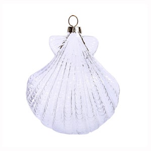 May include: A clear glass Christmas ornament shaped like a seashell. The ornament has a silver loop for hanging.