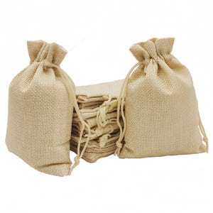 May include: Beige burlap drawstring bags. Two bags are upright, with a stack of folded bags in the background. The bags have a textured weave and a natural, neutral colour. The drawstring is a lighter beige.