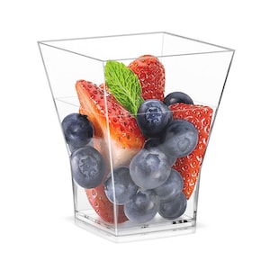 Op de afbeelding: Duidelijke vierkante plastic bekers gevuld met verse blauwe bessen en aardbeien. De bekers zijn perfect om desserts of hapjes te serveren.