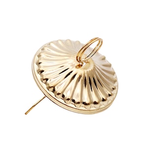 May include: A gold-coloured push pin with a circular, fluted head and a small ring attached. The pin has a long, slender point. The design is simple and elegant.
