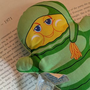 May include: A vintage green and yellow plush toy in the shape of a mitten with a cartoon face. The toy has a green striped pattern and a yellow face with blue eyes. The text "Myrtle - 1971" is visible in the background.
