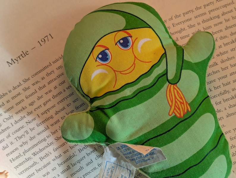 May include: A vintage green and yellow plush toy in the shape of a mitten with a cartoon face. The toy has a green striped pattern and a yellow face with blue eyes. The text "Myrtle - 1971" is visible in the background.