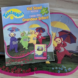 May include: A colourful Teletubbies jigsaw puzzle featuring the four main characters: Tinky Winky, Dipsy, Laa-Laa, and Po. The puzzle is made up of large, easy-to-handle pieces and is designed for children. The box features the Teletubbies logo and the text "Kid Sized Puzzle" in English and French.