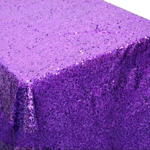 May include: A purple sequin tablecloth. The tablecloth is made of a soft, shimmery fabric with a subtle sheen.