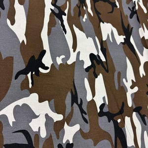 May include: Camouflage fabric with a brown, gray, and white pattern. The pattern is abstract and resembles a woodland scene.