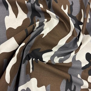 May include: Camouflage fabric in brown, gray, and white colors. The fabric has a classic camouflage pattern with irregular shapes.