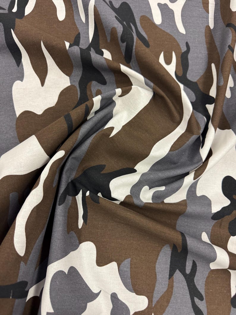 May include: Camouflage fabric in brown, gray, and white colors. The fabric has a classic camouflage pattern with irregular shapes.