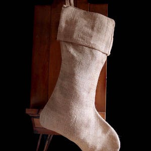 May include: A beige burlap Christmas stocking hanging on a wooden easel.