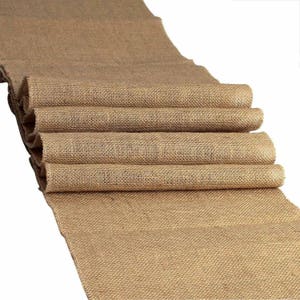 May include: A brown burlap runner, folded in thirds, with a rough texture. The runner is made of natural fibers and has a rustic look.