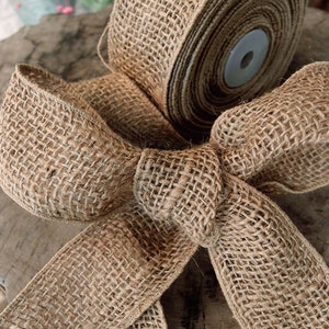 May include: A roll of natural brown burlap ribbon tied into a bow. The ribbon is woven with a textured pattern and has a frayed edge.