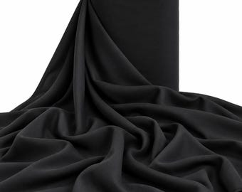 May include: A bolt of solid black fabric is shown with a portion of the material unrolled and draped in soft, flowing folds. The textile has a smooth, matte appearance and a consistent, deep black color throughout the entire piece.