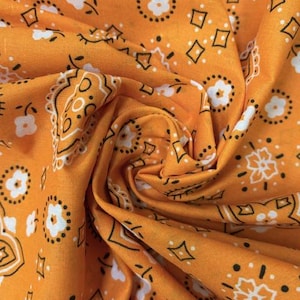 May include: A vibrant orange fabric featuring a repeating bandana pattern in white and black. The design consists of small white flowers, black diamond shapes, and intricate paisley-inspired outlines printed across the textured cotton material.