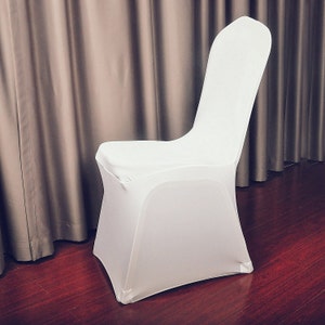 May include: A white chair cover made from a stretchy material. The cover is designed to fit over a standard chair, providing a clean and uniform appearance. The chair cover is shown against a neutral backdrop.