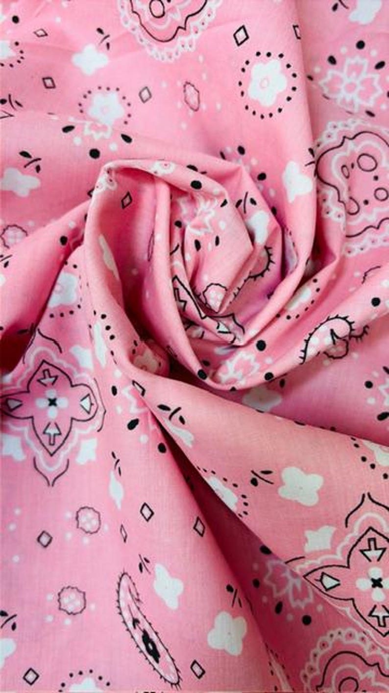 May include: A light pink fabric featuring a repeating bandana pattern in white and black. The design includes intricate floral motifs, small diamond shapes, and paisley elements printed across the surface of the soft, folded textile material.