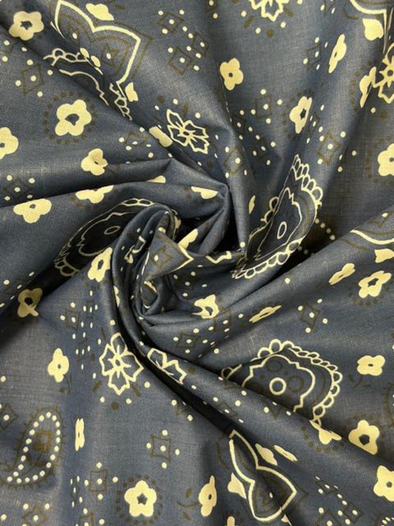 May include: A dark blue fabric featuring a repeating pattern of cream-colored floral motifs, paisley shapes, and small geometric dots. The textile is gathered in the center, creating folds that highlight the intricate, symmetrical print design.