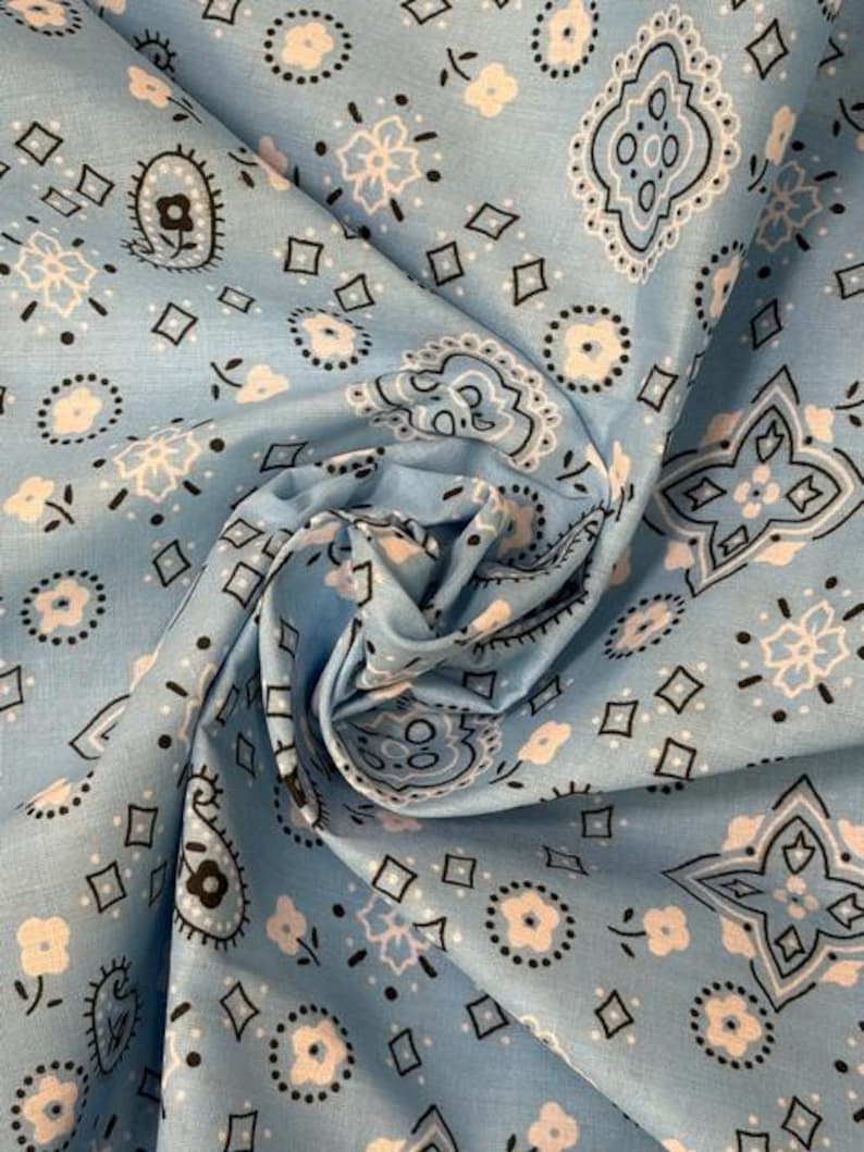 May include: A light blue fabric featuring a repeating bandana pattern in white and black. The design includes small floral motifs, geometric diamond shapes, and intricate paisley-inspired swirls arranged across the surface of the material.