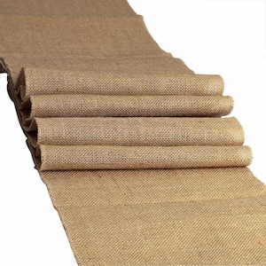May include: A brown burlap runner, folded in thirds, with a rough texture. The runner is made of natural fibers and has a rustic look.