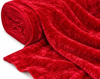 May include: A large roll of vibrant red crushed velvet fabric. The material features a distinct textured surface with light-reflecting highlights and deep shadows, showing the characteristic crinkled appearance of the fabric as it unrolls.