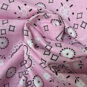 May include: A light pink fabric featuring a repeating bandana pattern in black and white. The design consists of small white flowers with black dotted outlines, interspersed with black diamond shapes and intricate floral motifs arranged in a classic layout.