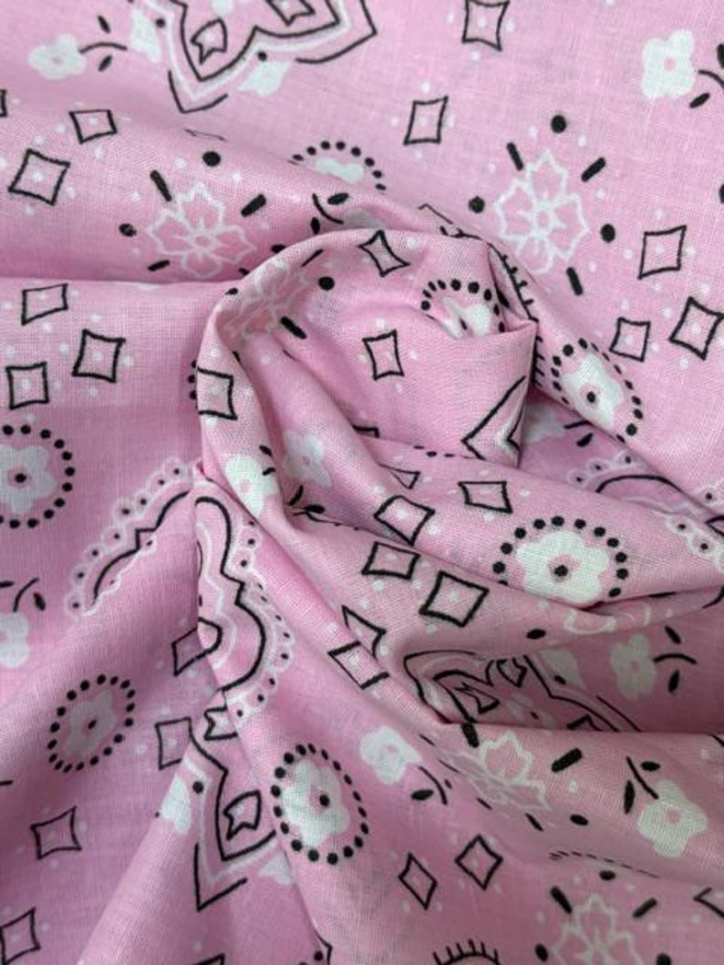 May include: A light pink fabric featuring a repeating bandana pattern in black and white. The design consists of small white flowers with black dotted outlines, interspersed with black diamond shapes and intricate floral motifs arranged in a classic layout.